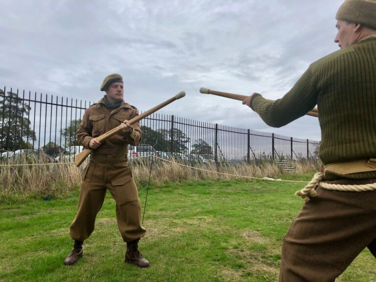 Two men in World War two uniforms facing off against each other with wooden bayonet trainers as part of a reenactment event