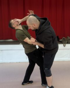 Two men wrestling the one on the right has his hand on the others face while kneeing him.