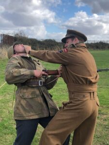 A man in British uniform doing a strike to another man in German uniforms face as part of a WW2 reenactment