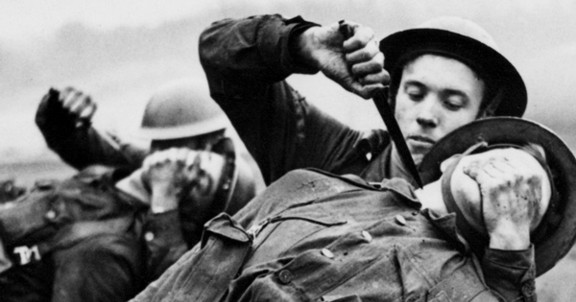 A British soldier practicing a sentry elimination on another British soldier in WW2. The image is black and white and the soldier practicing is covering the nose and mouth of his partner and has a knife to his throat