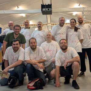 A group photo of Battalion Martial Arts York after their Christmas party doing knife fighting with red pens the group is wearing white T shirts covered in red marks from the pens