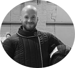 A Picture of an instructor of Battalion Martial Arts Davide smiling at the camera in a black padded Jacket made for Fencing